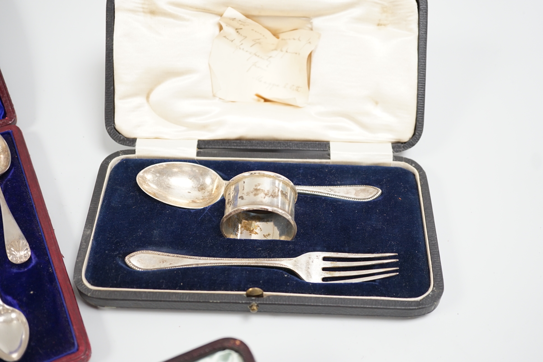 A cased George V silver christening trio, two cased sets of silver teaspoons, including set of twelve with sugar tongs and a cased modern silver mounted presentation cigarette box.